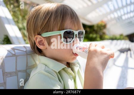 Porträt eines fröhlichen kleinen Jungen mit Sonnenbrille, der Saft trinkt Stockfoto
