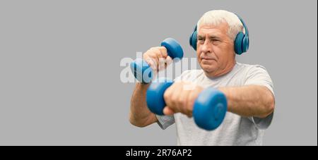 Senior-Mann, der Banner trainiert. Grauer Stusio-Hintergrund. Person, die Kurzhanteln hebt. Alter Mann, der Sport macht. Gesunder Lebensstil. Aktives Sporttraining. Älter Stockfoto