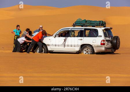 Der Gruppenführer ermutigt Sie, während die Reisegruppe sich alle anschließt, um ihr Fahrzeug mit Allradantrieb aus dem weichen Sand des sudanesischen herauszuschieben Stockfoto