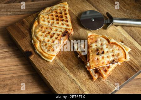 Trendige, hausgemachte Pizza-Waffel mit Tomatensauce, Peperoni, Oliven und Parmesankäse auf einem Schneidebrett Stockfoto