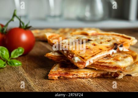 Scheiben hausgemachter Pizza Waffel mit Tomatensauce, Peperoni, Oliven und Parmesankäse auf einem Schneidebrett Stockfoto