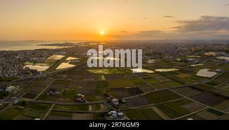 Luftaufnahme der niedrigen Sonne am Himmel über den Feldern am Rand einer Kleinstadt an der Küste Stockfoto