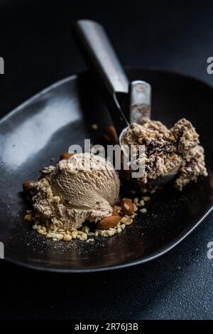 Draufsicht auf die schwarze Keramikplatte mit einer Schaufel Eiscreme neben einer Schaufel Schokoladeneis mit Erdnüssen und Nüssen Stockfoto