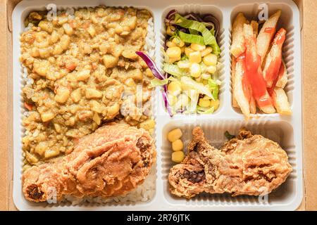 Die Bento-Box enthält Curryreis, Hähnchenschenkel, pommes frites und Gemüsesalat. Stockfoto