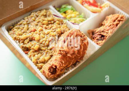 Die Bento-Box enthält Curryreis, Hähnchenschenkel, pommes frites und Gemüsesalat. Stockfoto