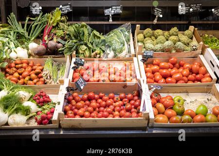 Gemischtes frisches, reifes Bio-Tomaten-Gemüse in offenen Kartons mit Preisschildern für jedes Gemüse im Einzelhandelsgeschäft Stockfoto