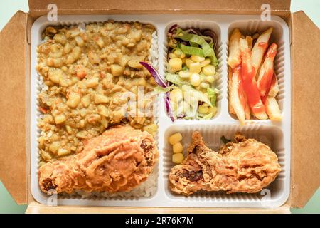 Die Bento-Box enthält Curryreis, Hähnchenschenkel, pommes frites und Gemüsesalat. Stockfoto