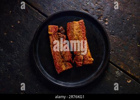 Blick von oben auf die schmackhaften, fetten, gegrillten Schweinerippchen, serviert auf einem schwarzen Teller auf einem Holztisch Stockfoto