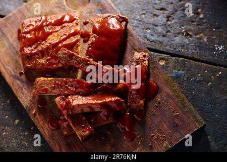 Blick von oben auf schmackhafte gegrillte Schweinerippchen mit Ketchup, serviert auf Holzbrett in der Küche Stockfoto