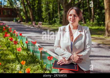 Porträt einer glücklichen Geschäftsfrau mit Tablet im Spring Park. Landschaftsdesignerin genießt die Ergebnisse blühender Blumenbeete im öffentlichen garten Stockfoto