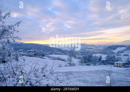 Schneesturm in den Bergen bei Sonnenuntergang. Schneebedeckte Hügel, Berge, Dorf, Natur, Horizont. Natürlicher Hintergrund. Appennino-Tosco-emiliano Stockfoto