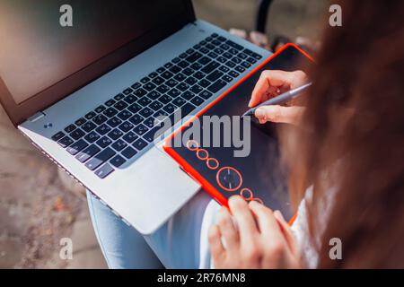 Frau, die im Freien mit Notebook und Tablet arbeitet. Grafikdesigner, der Remote arbeitet. Zeichnen mit dem Stift. Draufsicht Stockfoto