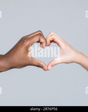 Menschen mit unterschiedlichen Hautfarben legen ihre Hände zusammen und bilden Herzform auf weißem Hintergrund. Nahaufnahme weiblicher und männlicher Hände unterschiedlicher Hautfarbe Stockfoto