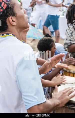 Eine lebhafte und fröhliche Szene von Menschen jeden Alters, die gemeinsam Musikinstrumente an einem sonnigen Strand spielen Stockfoto