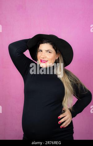 Eine schöne schwangere Frau, die ein schickes schwarzes Outfit trägt und selbstbewusst lächelt Stockfoto