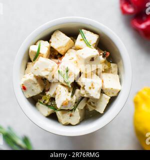 Blick von oben auf marinierte Feta-Käsewürfel in einer Zimt, Käsewürfel marinieren in Kräuteröl, flache Lage aus Feta-Käse in Olivenöl in einer weißen Zimt Stockfoto