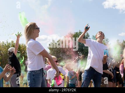 Kaukasische Erwachsene Und Kinder Feiern Das Holi Color Festival Und Werfen Farbige Farbstoffe In Die Luft. Gruppe Von Kindern, Eltern Spielen Mit Paint Outdoor In Park Stockfoto