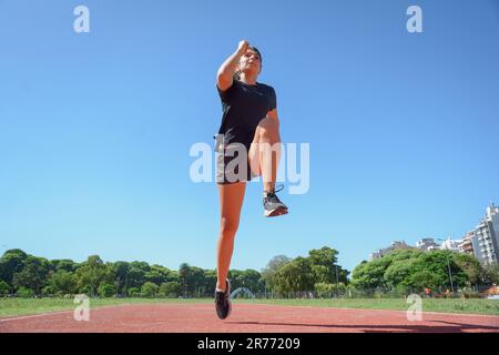 Weitwinkel-Vorderansicht einer jungen argentinischen latina in schwarzer Sportbekleidung, Outdoor-Training bei Sprüngen mit einem Bein, Sportkonzept, Kopierbereich. Stockfoto