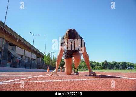 Vorderansicht einer Frau auf der Rennstrecke in Startposition, mit Himmel im Hintergrund und Kopierraum. Stockfoto