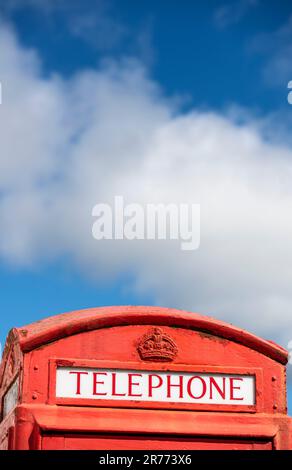 Eine ikonische rote britische Telefonzelle kontrastierte mit einem blauen Himmel und weißen Wolken Stockfoto