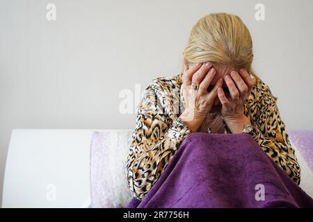 Verängstigte alte Frau, Opfer von Gewalt und Aggression in ihrem Schlafzimmer. Der Schrecken einer Ehefrau bei häuslicher Gewalt. Psychische Gesundheitsschmerzen Stockfoto