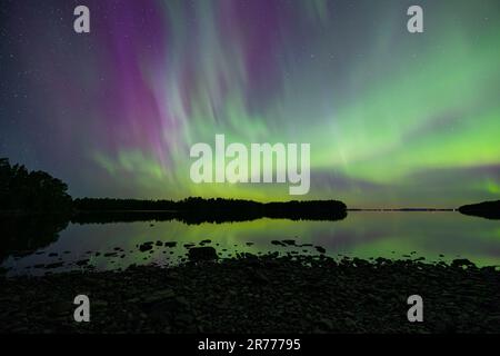 Ein majestätischer Blick auf die Aurora Borealis oder die Nordlichter, die den Nachthimmel über einem ruhigen See erleuchten Stockfoto