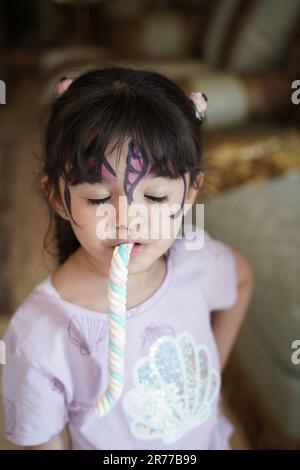 Unartige Kinderreaktion oder Gesichtsausdruck. Unartiges kleines Mädchen, das Süßigkeiten mit Gesichtsfarben isst. Stockfoto