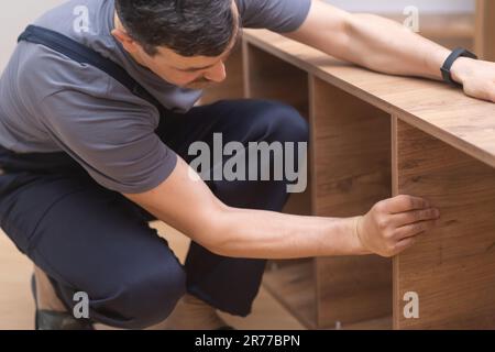 Kundenspezifische Möbelherstellung und Fixiermann in Overalls zur Installation von Regalen auf Holzregalen