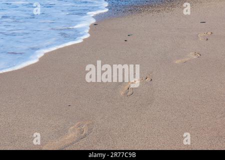 Fußabdrücke auf dem sandigen Strand hinter sich gelassen Stockfoto