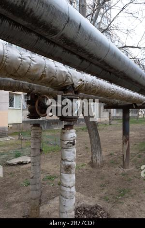 Alte Hauptluftheizung mit ausgeschaltetem Ventil. Konzept von Verzweiflung, Armut, Konkurs und Verwüstung. Das Heizrohr wird im Freien über dem Boden verlegt. Stockfoto