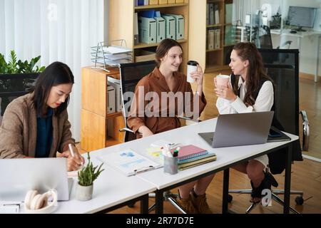Gruppe von Kollegen, die miteinander sprechen und während der Pause Kaffee am Tisch trinken Stockfoto