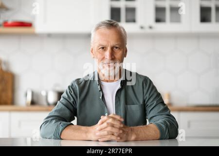 Porträt eines gutaussehenden Seniorenmannes, der in der Küche sitzt Stockfoto