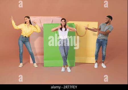 Positive multiethnische Millennials, die sich vor großen Einkaufstaschen posieren Stockfoto