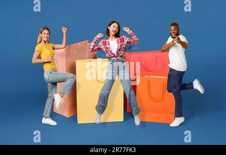 Fröhlicher, multiethnischer Mann und Frau, die neben Einkaufstaschen springen Stockfoto