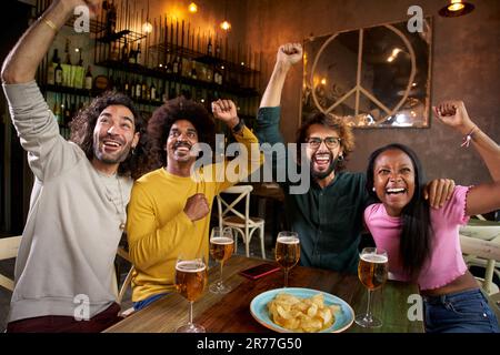 Gemischtrassige Gruppe von Fußballfreunden, die in einer Bar mit fernseher das Ziel des Sieges feiern Stockfoto