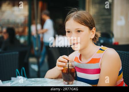 Ein kleines Mädchen trinkt Eistee im Café draußen Stockfoto