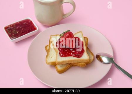 Teller mit leckerem Toast mit Erdbeermarmelade und Milch im Pitcher auf pinkfarbenem Hintergrund Stockfoto