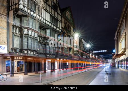 Nachts legt ein Bus leichte Wege vor den restaurierten Tudor-Holzfassaden von Geschäften und Büros in der High Street von Exeter ab. Stockfoto