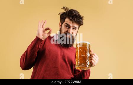 Ein betrunkener Mann mit Bart und einem Becher Bier, der das Schild in Ordnung zeigt. Schlechte Angewohnheiten. Alkoholismus. Stilvoller Mann, der Craft-Bier vom Fass trinkt. Alkohol, Brauerei. Bier Stockfoto