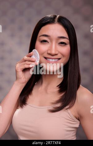 Kosmetologisch lächelndes asiatisches Modell, das Hautpflege-Routine-Porträt macht. Fröhliche junge, schöne Frau, die mit Mikellarwasser die Hautpflege reinigt und in die Kamera schaut Stockfoto