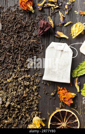 Zusammensetzung von trockenem schwarzen und grünen Tee, Teebeutel, getrockneten Zitrusscheiben und trockenen Hibiskusblumen auf dunklem Holzhintergrund von oben. Verschiedene Arten von Stockfoto