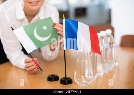 Vorbereitung auf Geschäftsverhandlungen - Frau setzt kleine Flaggen von Ländern Frankreichs und Pakistans auf den Tisch Stockfoto