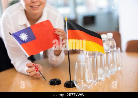 Vorbereitung auf Geschäftsverhandlungen - Frau setzt kleine Flaggen von Taiwan und Deutschland auf den Tisch Stockfoto