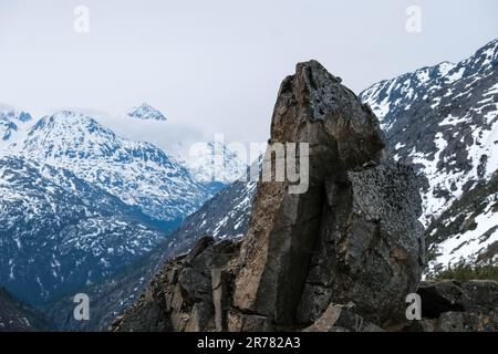 Großer, zerklüfteter Stein mit niedrigen Wolken und schneebedeckten Berggipfeln Stockfoto
