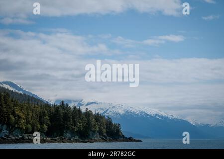 Niedrige Wolken über schneebedeckten Bergen und Meer in Alaska Stockfoto
