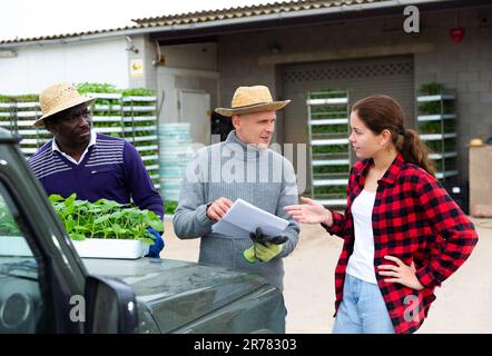 Mädchenmanagerin, die mit Arbeitern die Lieferung von Setzlingen auf die Farm diskutiert Stockfoto