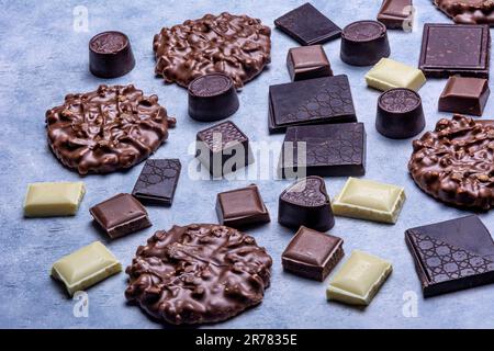 Verschiedene Schokoladenprodukte, die im Studio auf hellgrauem Hintergrund mit weißer Textur fotografiert wurden. Dunkle Schokolade, Milchschokolade, weiße Schokolade, C. Stockfoto