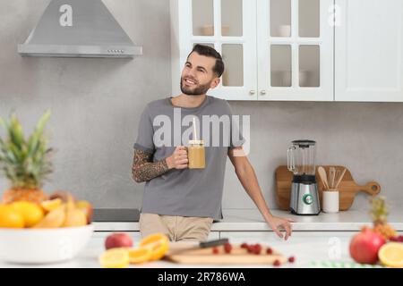 Hübscher Mann mit leckerem Smoothie in der Küche Stockfoto