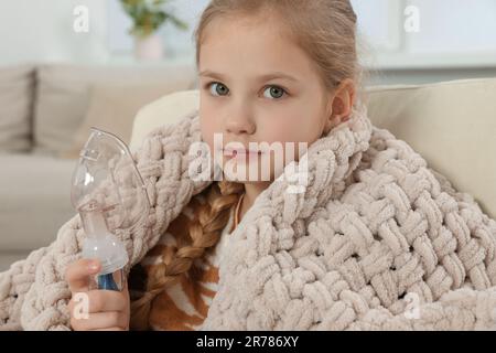 Ein kleines Mädchen hält einen Vernebler für die Inhalation zu Hause Stockfoto