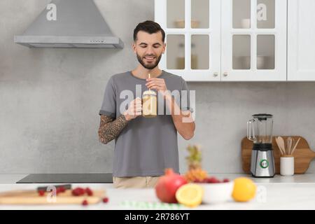 Hübscher Mann mit leckerem Smoothie in der Küche Stockfoto